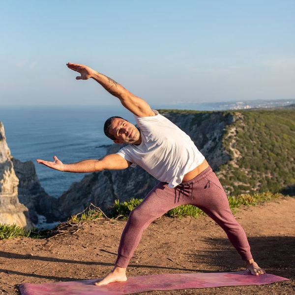 Man demonstrating a powerful warrior yoga pose on a cliff overlooking the ocean.